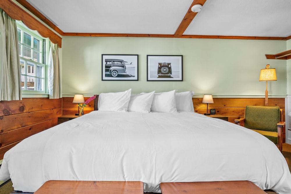 King bed, white bed cover, pine furniture, green walls, two photos above bed, and luggage tables at foot of bed