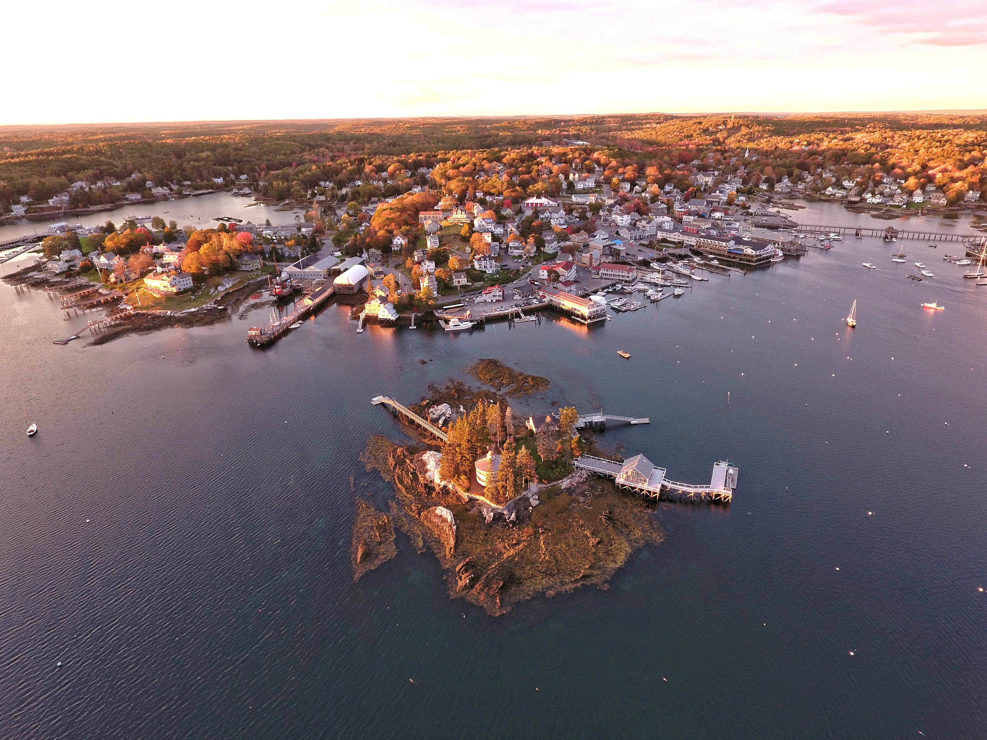 Aerial view of a large harbor town at the edge of a large body of water with a lighthouse on a nearby island