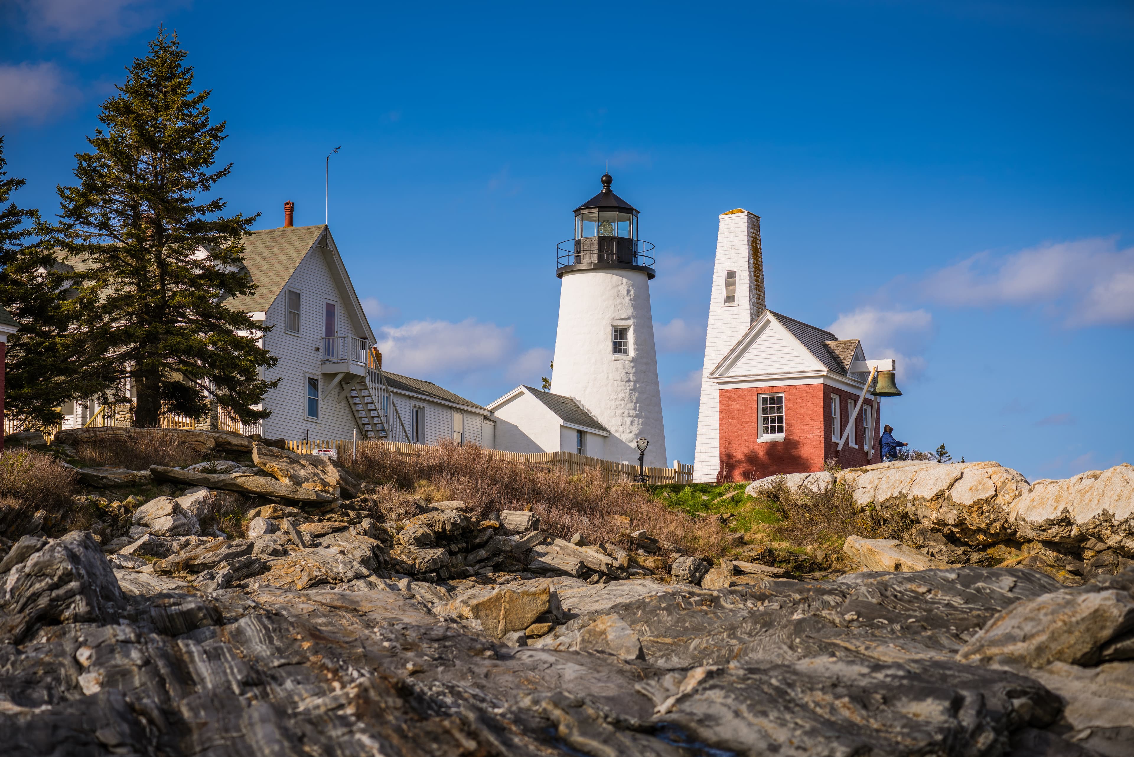 Large white lighthouse with a red outbuilding sitting at the edge of a rocky bluff