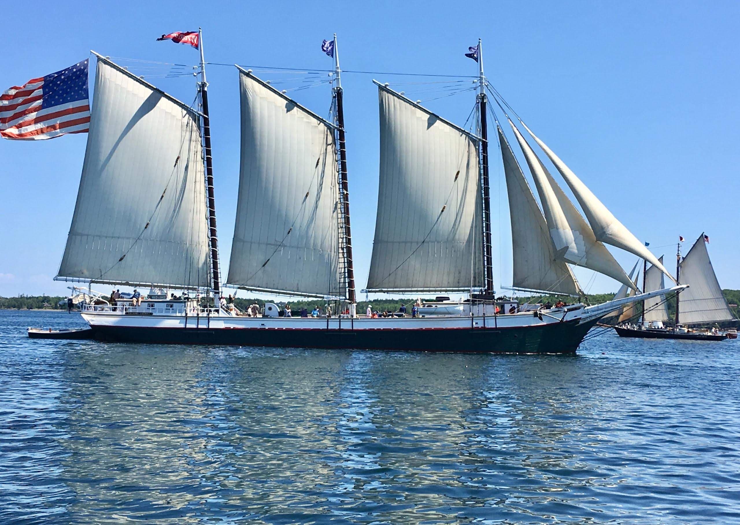 An expansive sailboat with six sails open in calm waters with a second sailboat behind