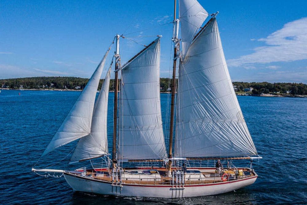 A large schooner sailboat with full sails up in the water with blue skies