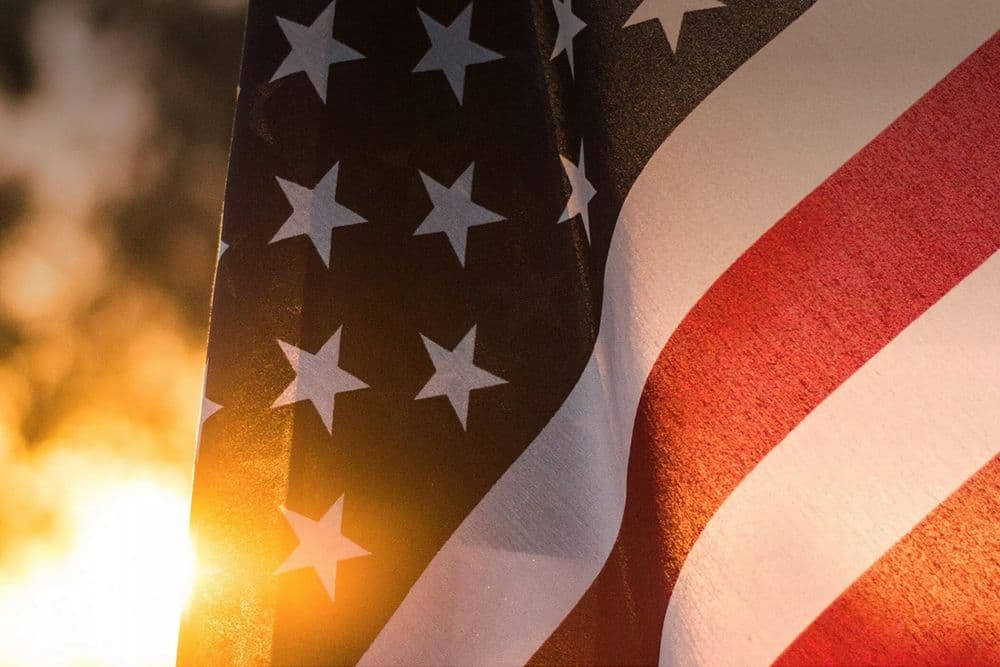 An American flag hanging outside with a burst of sunshine coming through