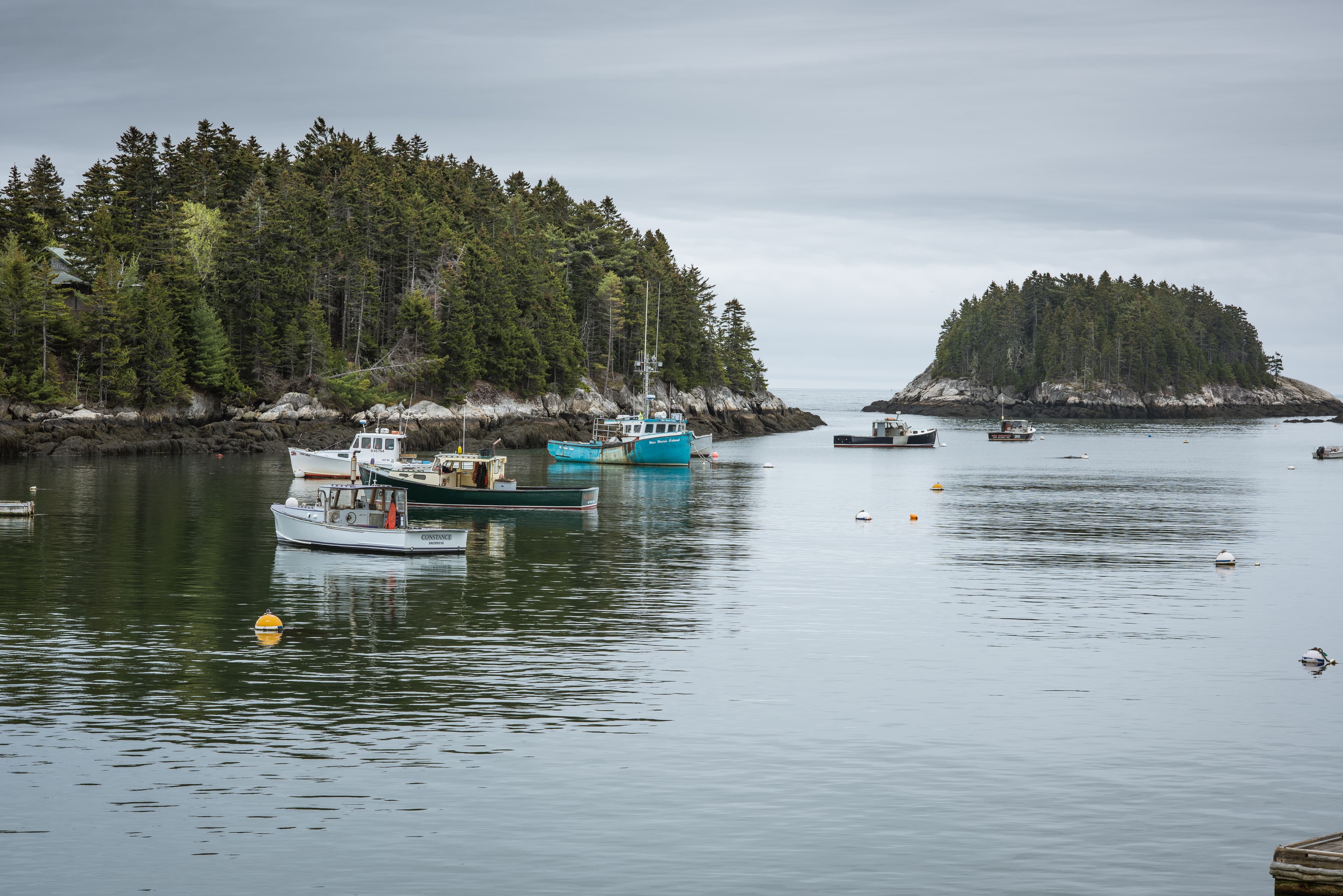 Large body of water with two rocky islands and six fishing boats anchored