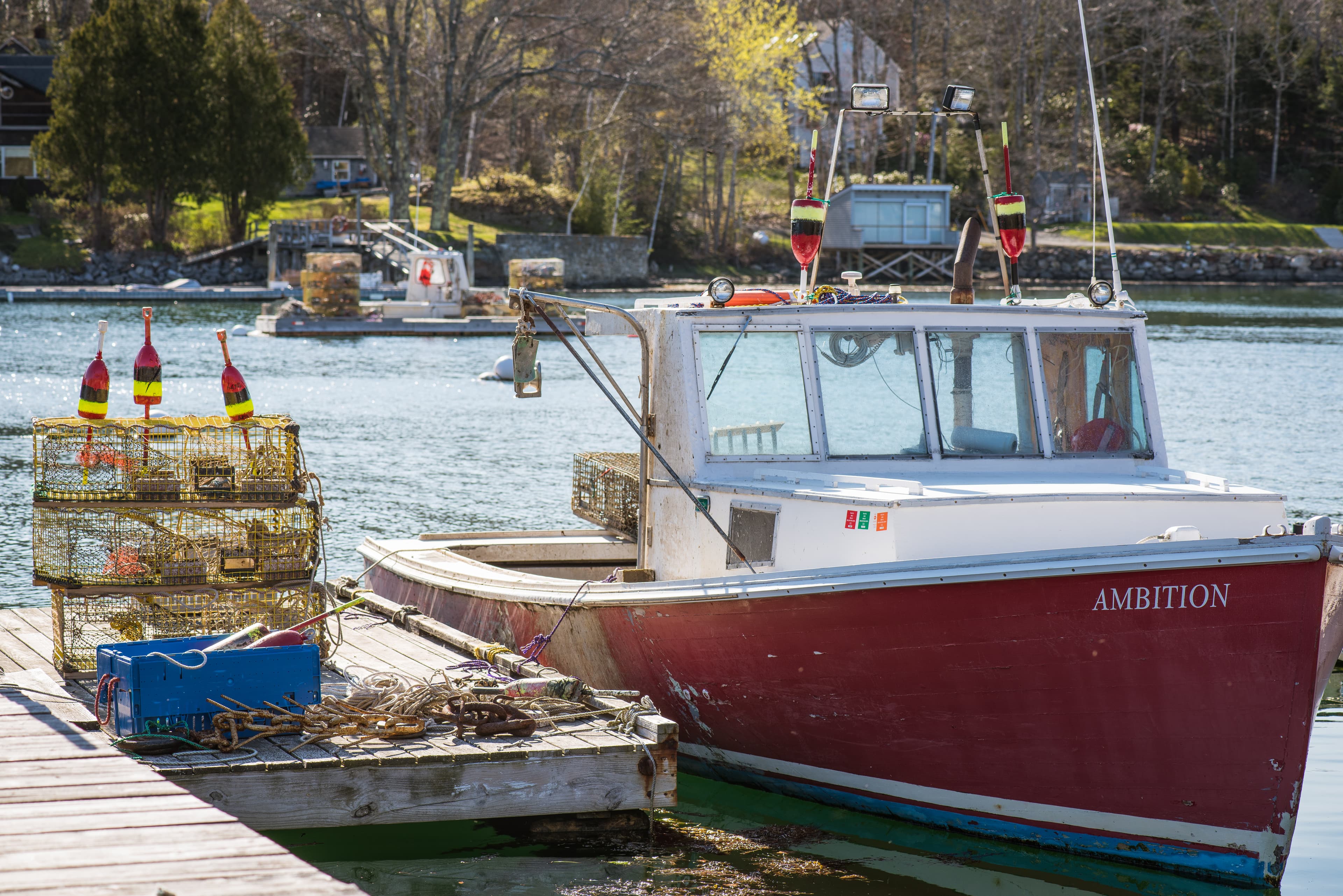 A red and white fishing boat tied to a dock with a stack of fishing pots