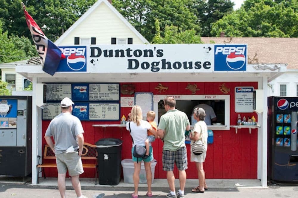 A small red and white hot dog and burger joint with people standing in line to order