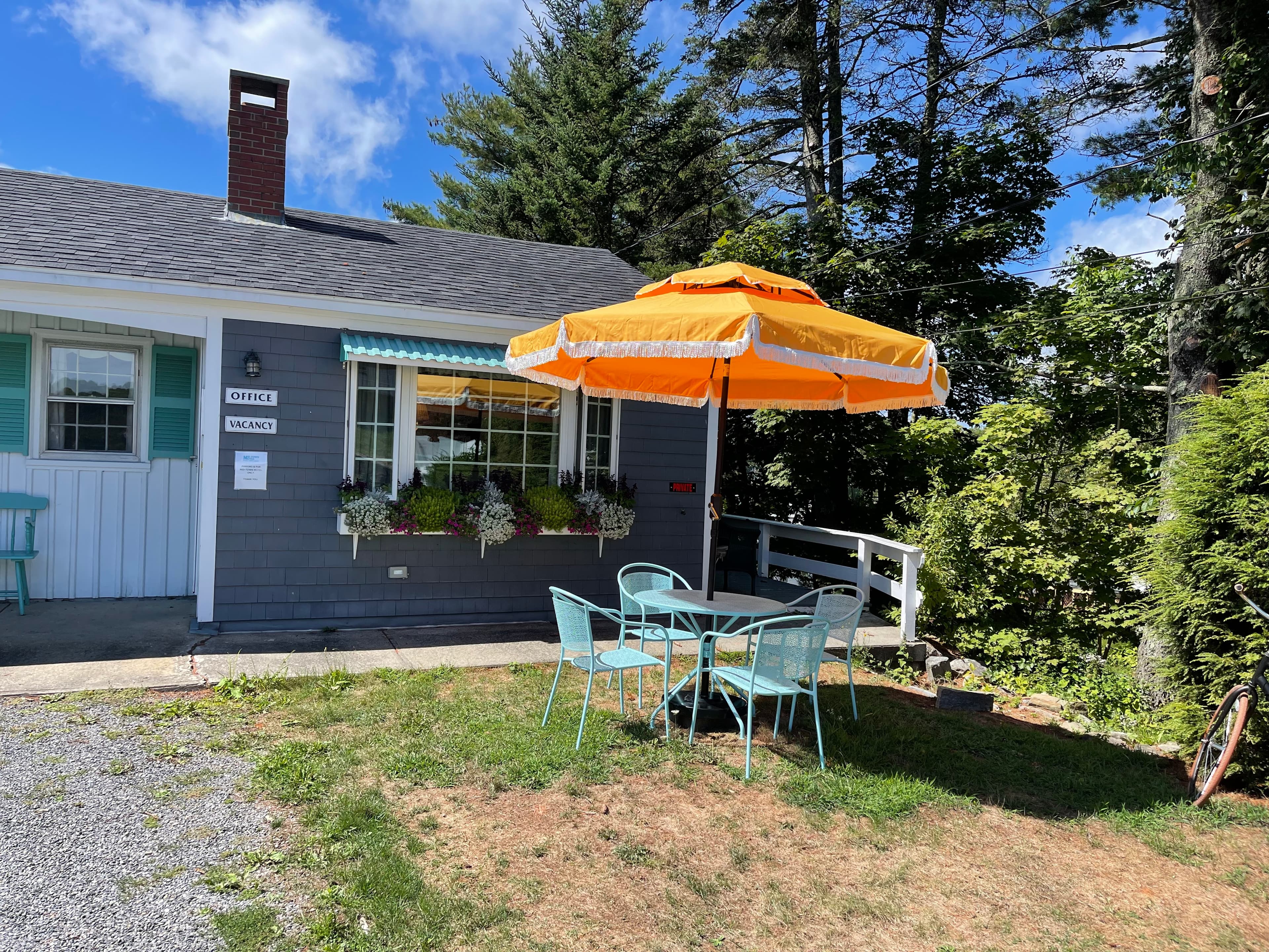 A small blue office building with a teal patio table with chairs and a yellow umbrella